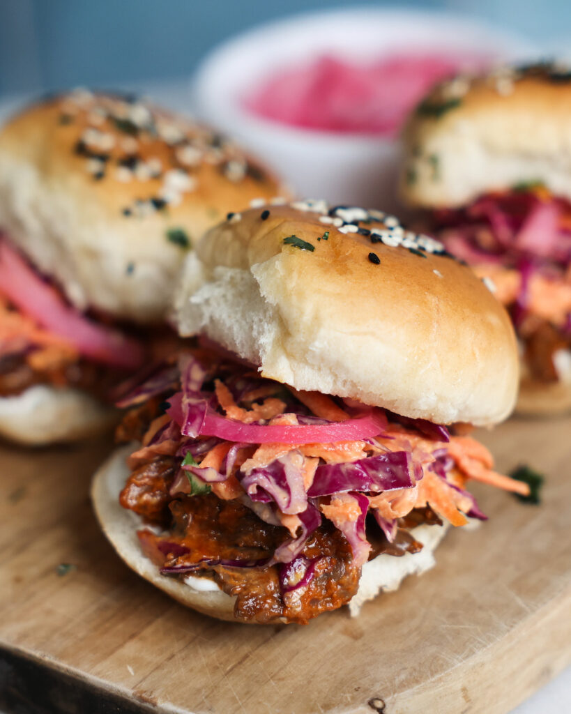 A close up of mushroom veggie sliders on a wooden cutting board with pickled red onions.