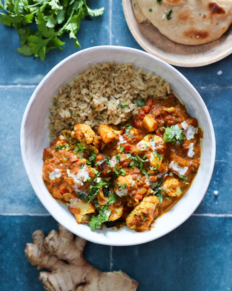 overhead of vegan tempeh tikka masala in a white bowl on a blue tile counter.