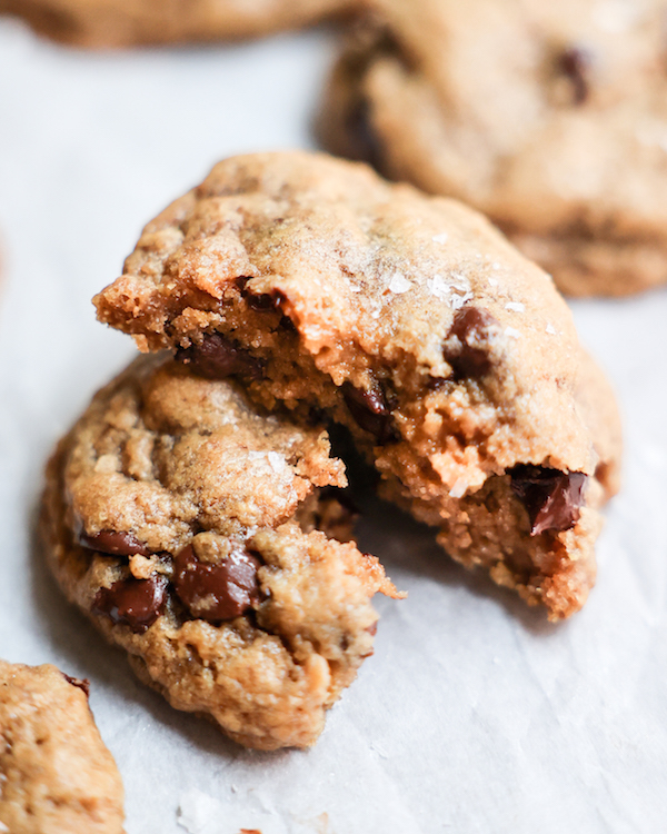 An up-close shot of a vegan chocolate chip cookie broken into two on a white counter.