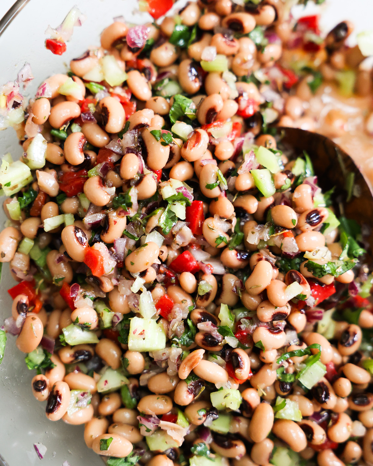 Black eyed pea salad in a glass bowl with wooden spoon