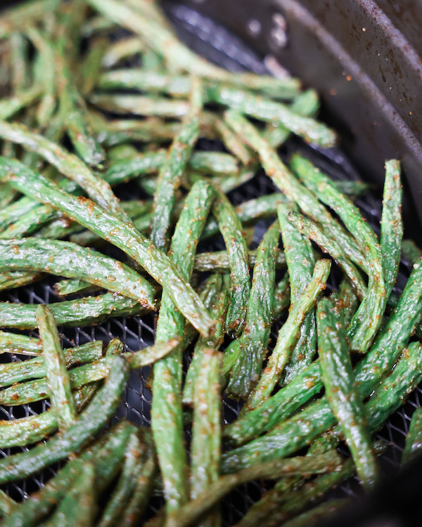 fried green beans in an air fryer basket