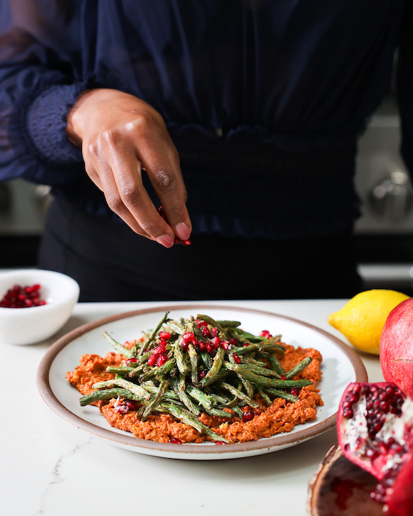 hand garnishing air fryer green beans with pomegranate seeds