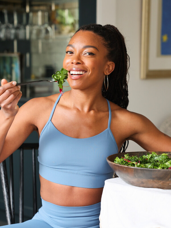 Jenne Claiborne eating a large salad at table wearing blue activewear