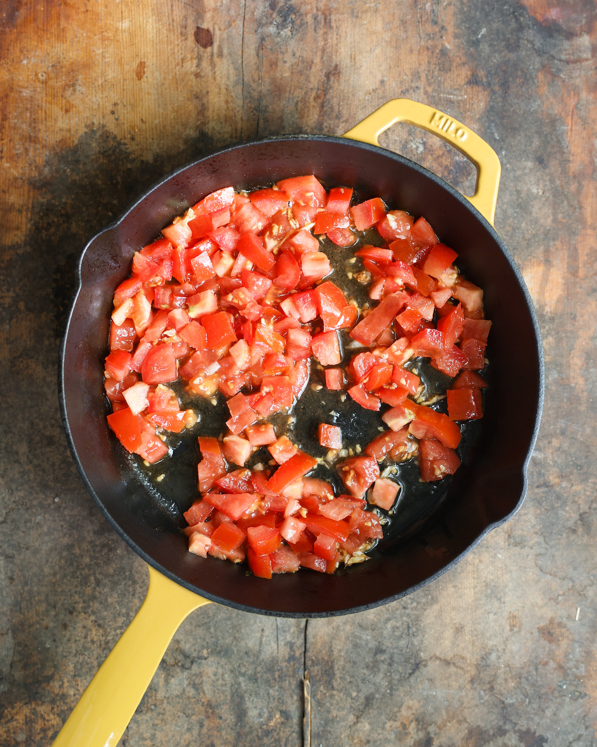 an overhead of diced tomatoes sautéing in a yellow skillet