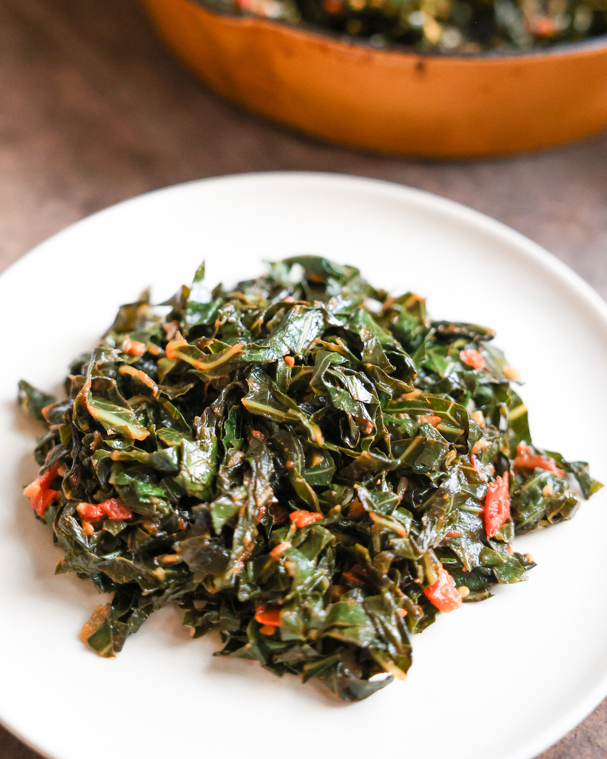 vegan collard greens on a white plate in front of a skillet