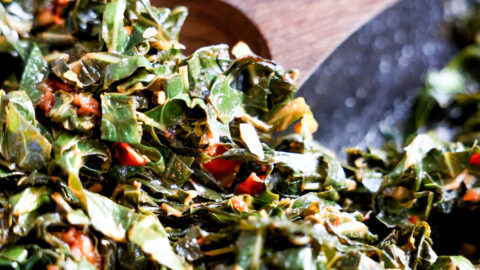 Wooden spoon scooping collard greens in a skillet.
