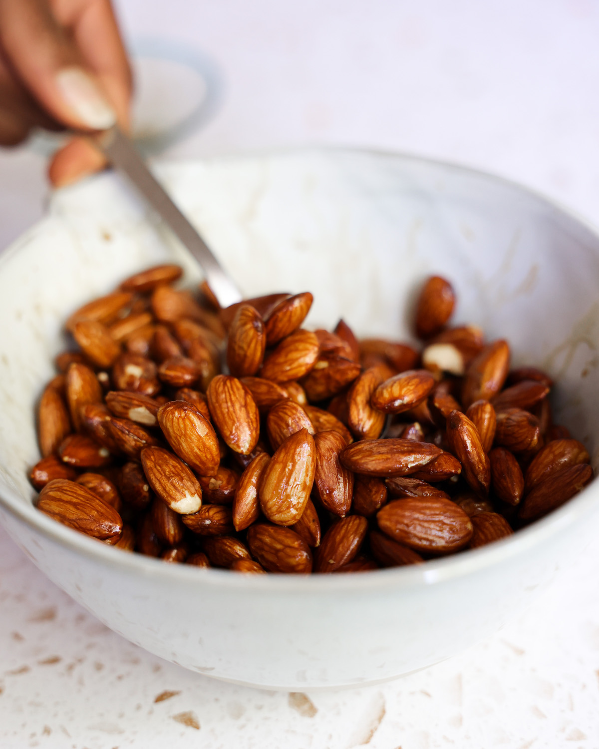 Stirring almonds with tamari in a white bowl before scooping out to drain.