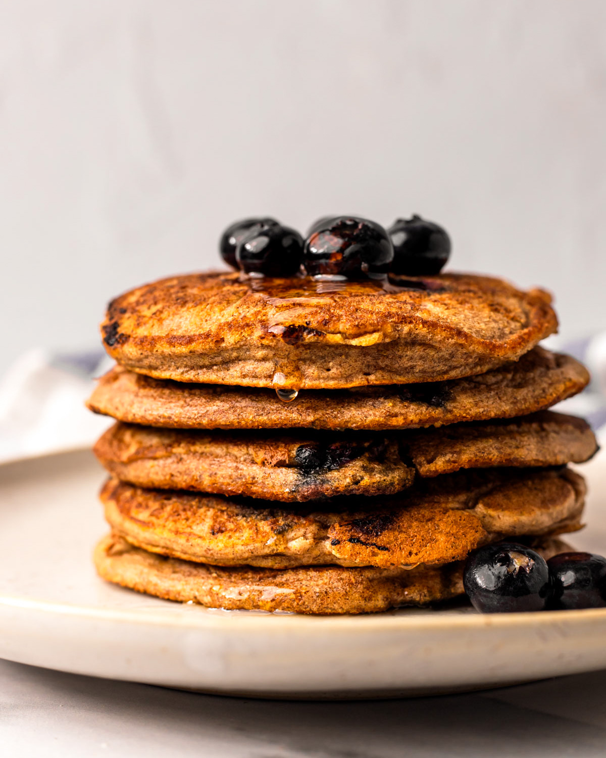 A side shot of a stack of vegan blueberry pancakes with a bit of maple syrup on top.