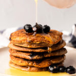 Drizzling a stack of the vegan blueberry pancakes with maple syrup.