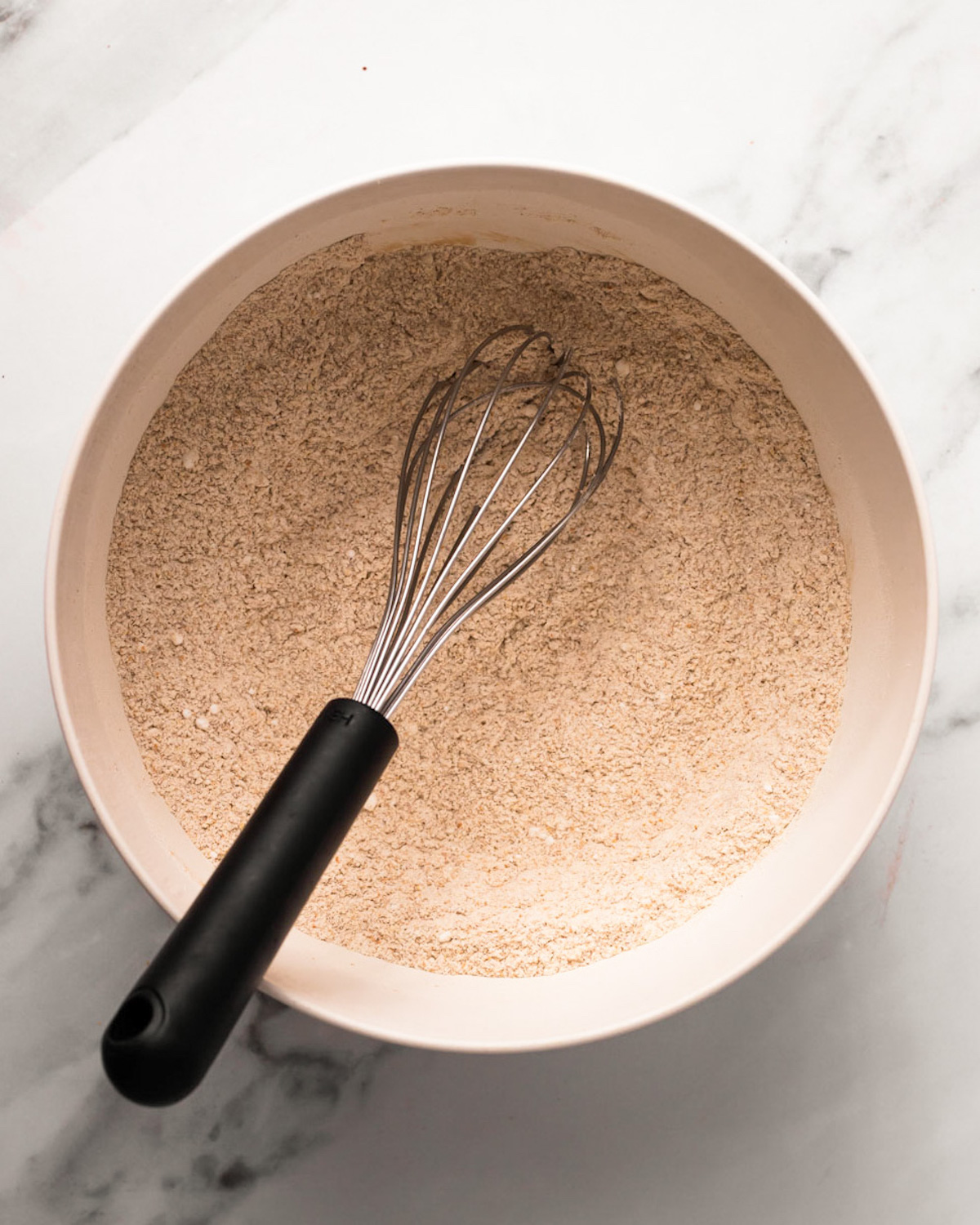An overhead shot of a bowl of whisked whole wheat flour with a whisk.