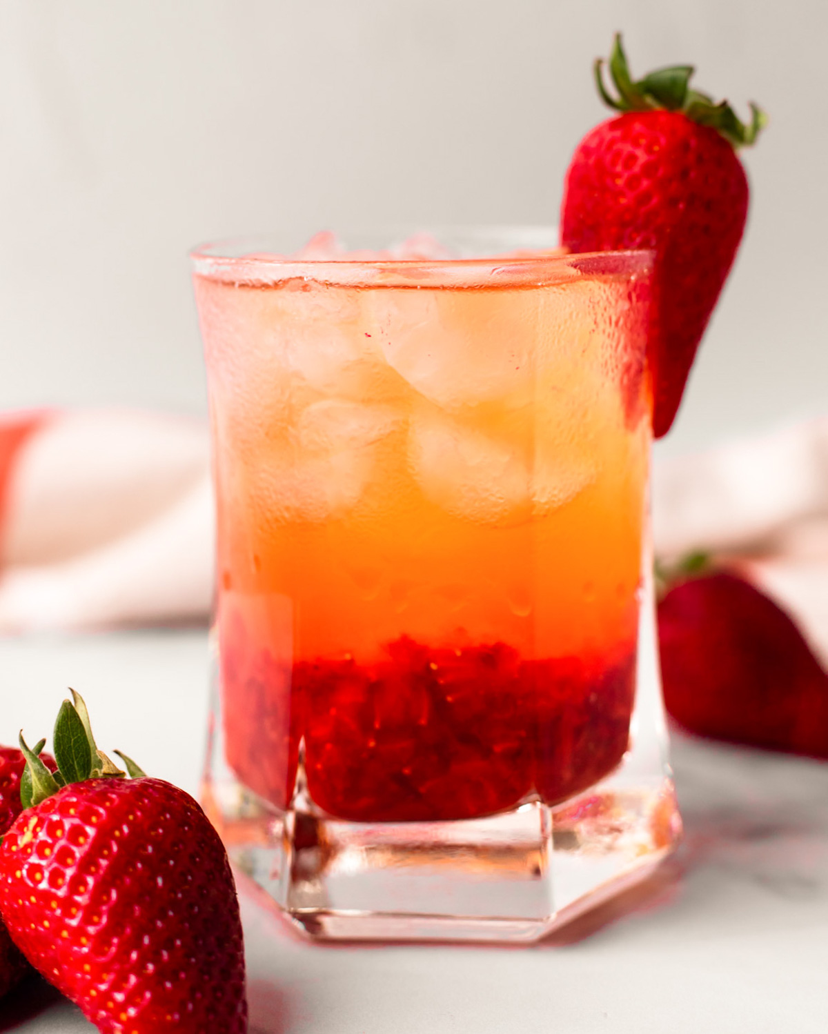 An up-close side shot of a glass of strawberry rose bramble on the counter with strawberries.