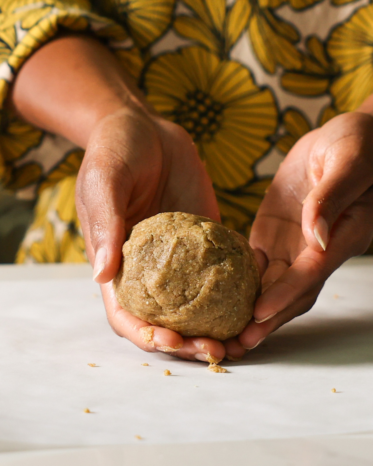 Two hands holding the ball of pumpkin seed cracker dough on the counter.