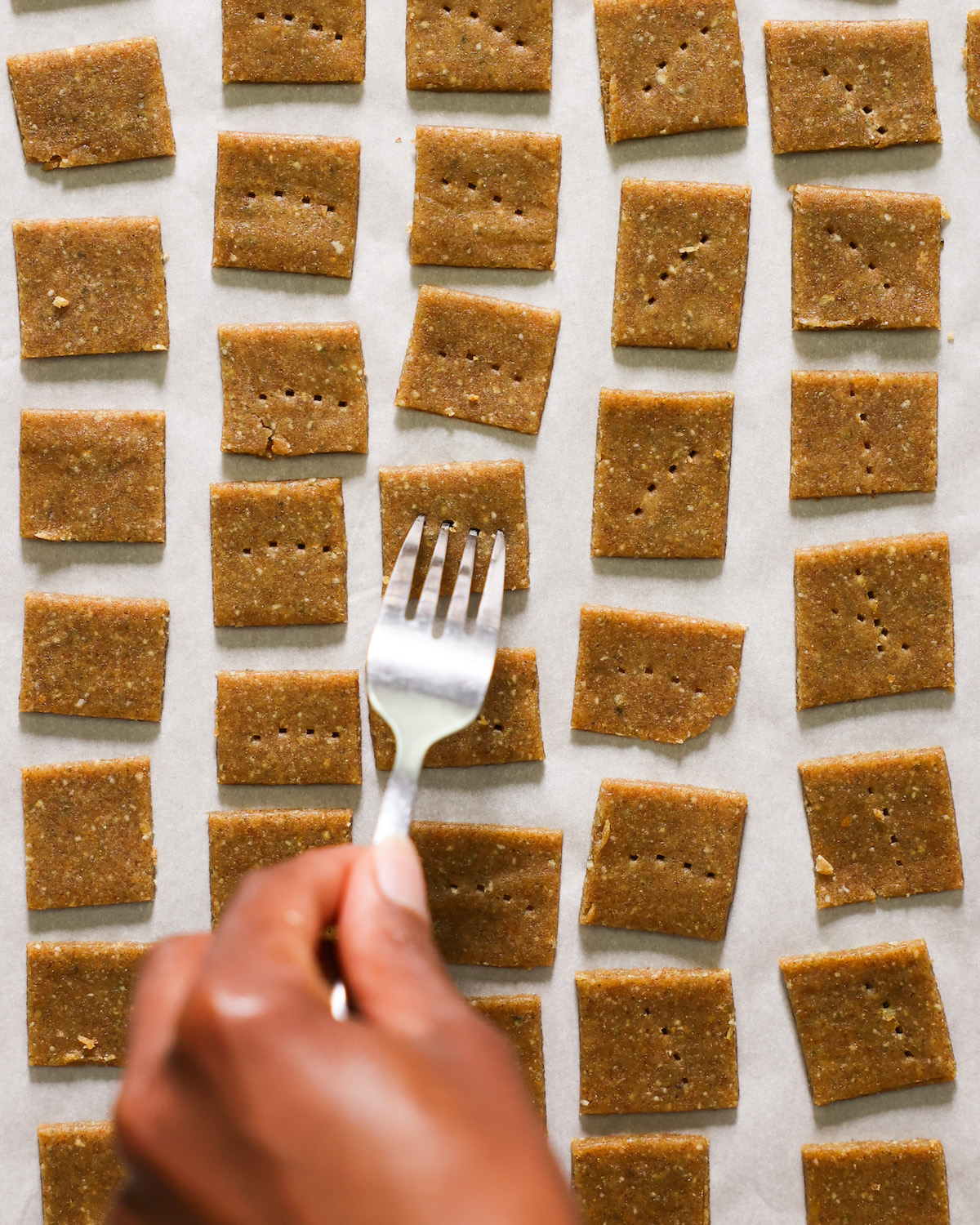 Poking holes in the pumpkin seed crackers with a fork before baking.