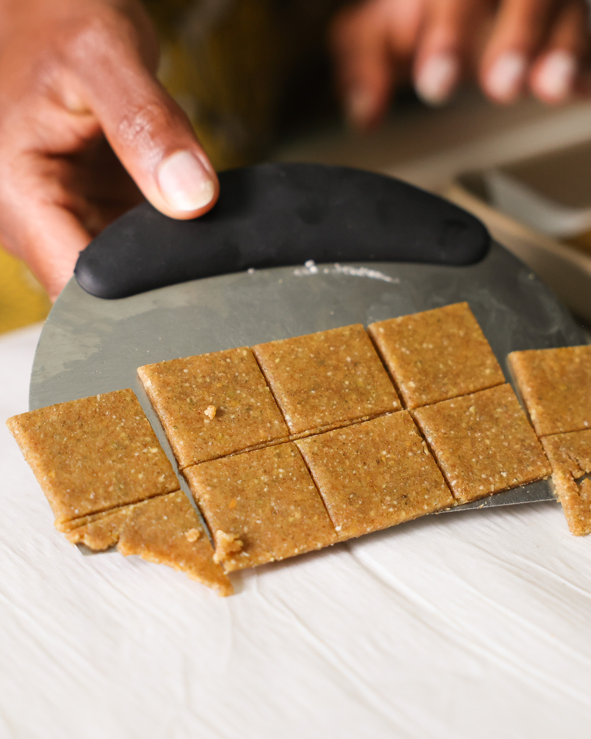 Scraping the "cheesy" pumpkin seed crackers off of the counter with a bench scraper.