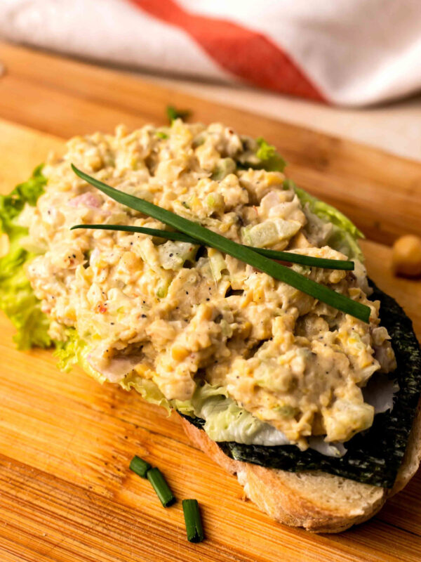 Vvegan chickpea salad on toast on a wooden cutting board.
