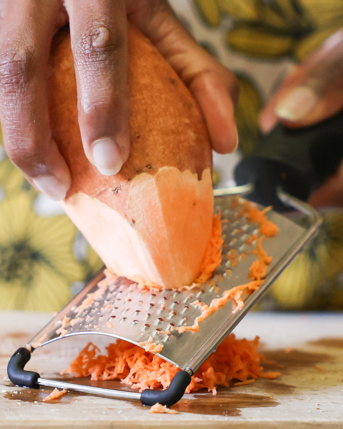 An up-close shot of a brown hand shredding a sweet potato on a cutting board.
