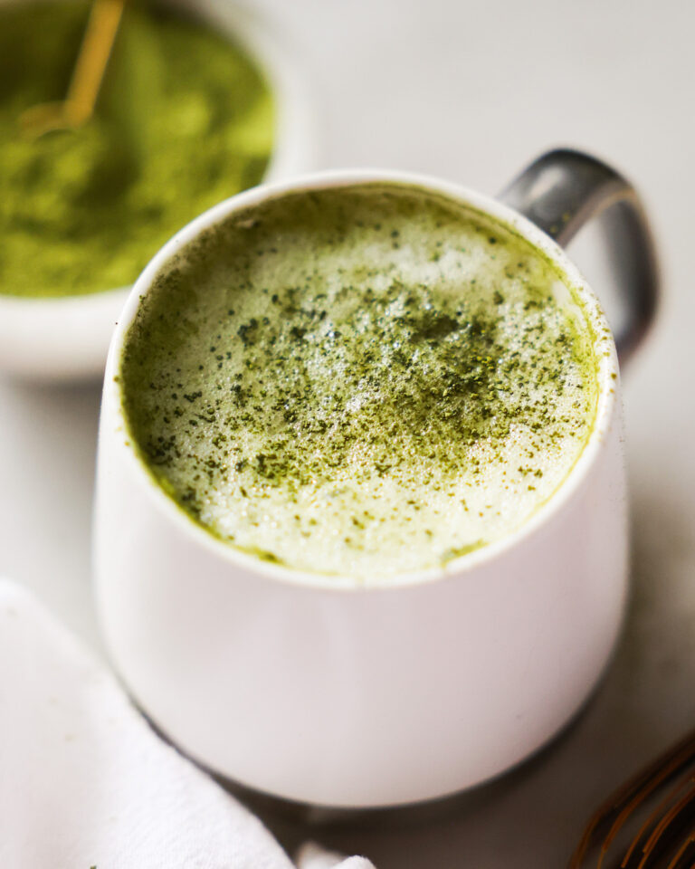 A close-up image of a mug of oat milk latte on the counter with a towel.