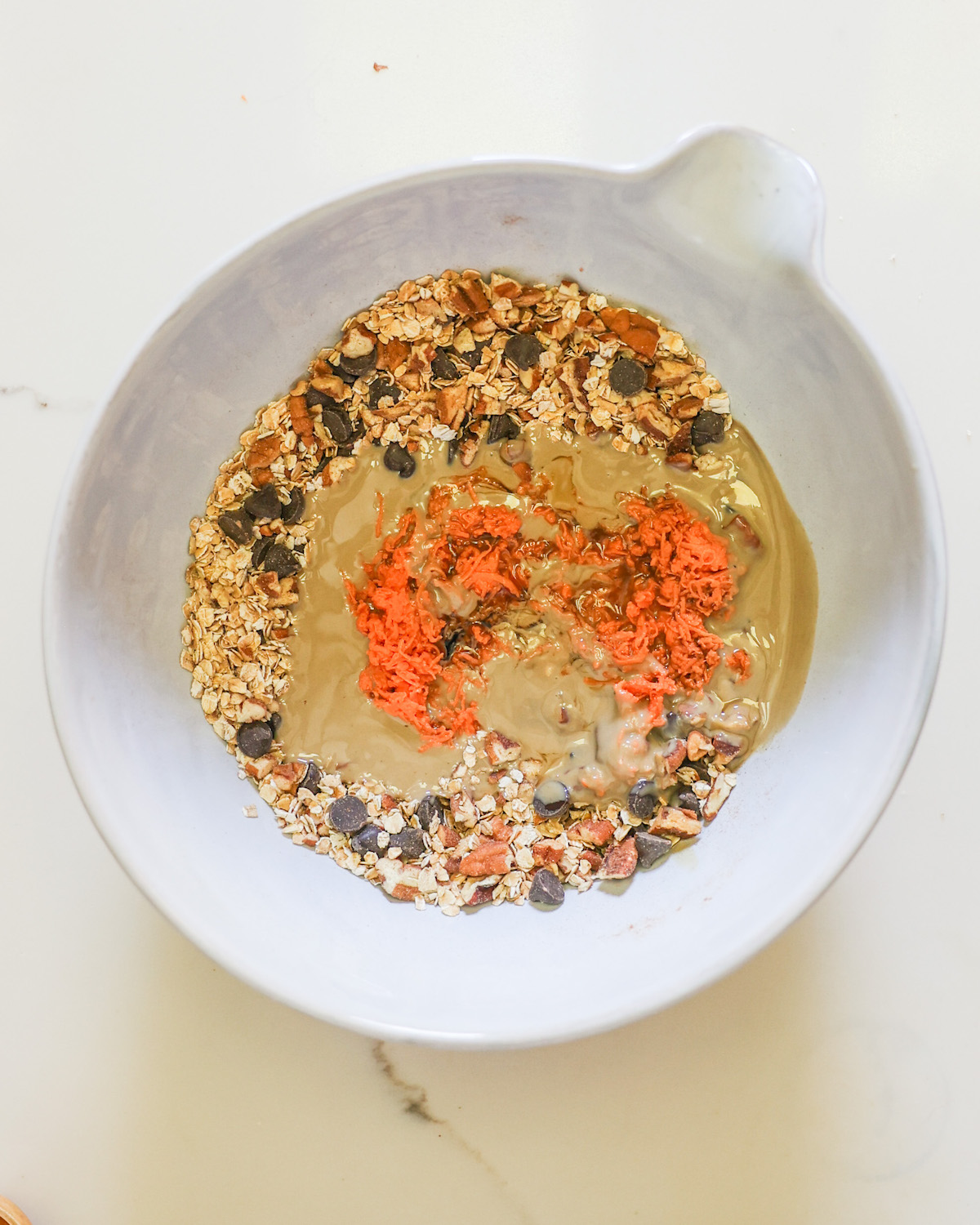 A mixing bowl of the oats, pecans, chocolate chips, tahini, and shredded sweet potatoes.