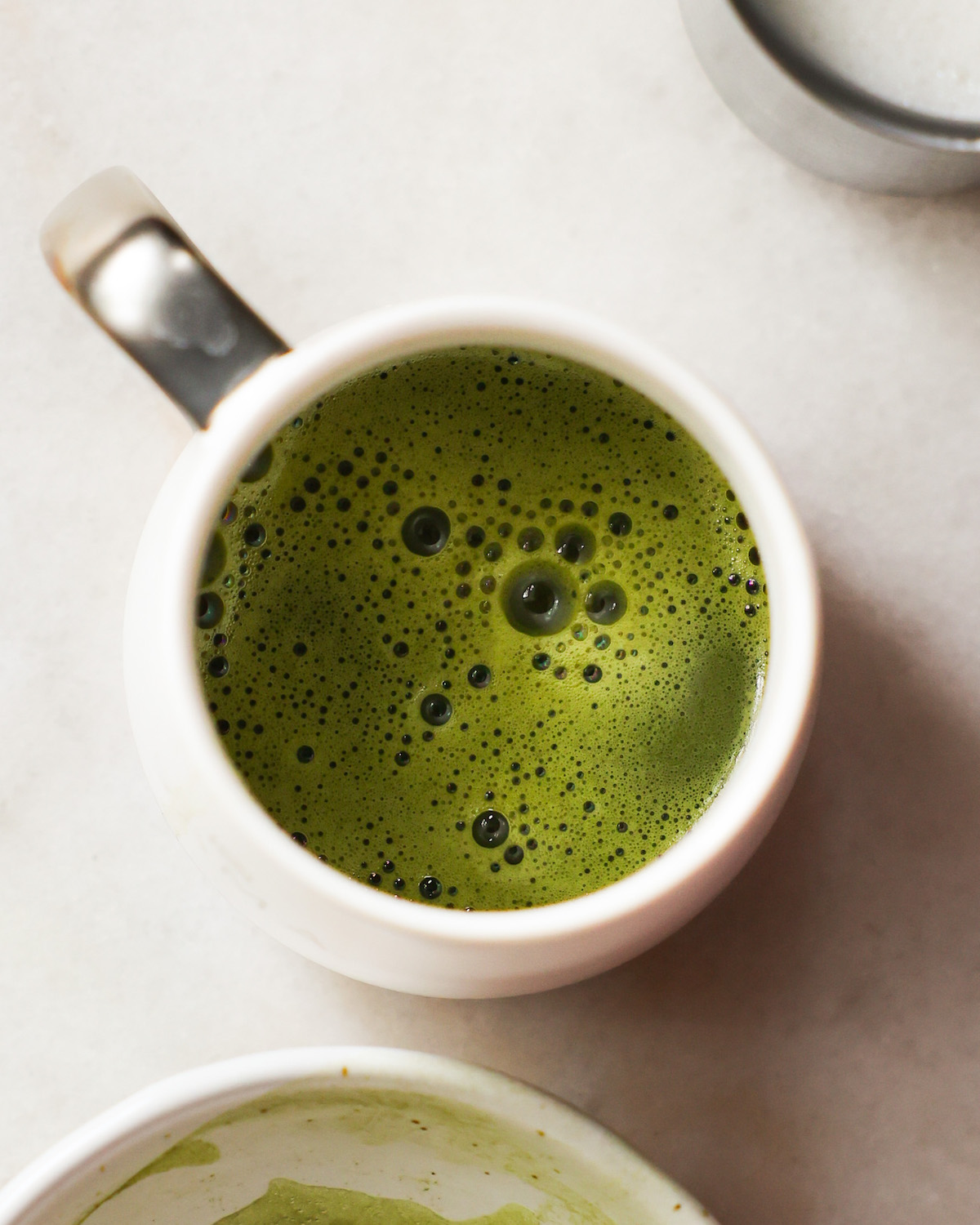 A close-up overhead shot of a white mug of matcha on the counter.