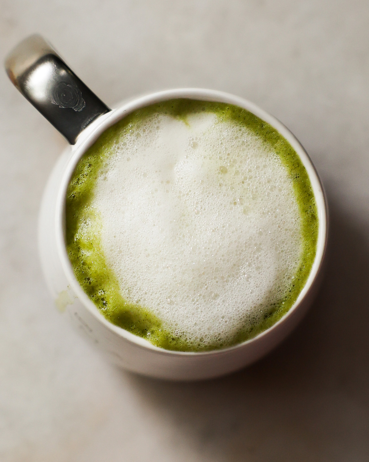 A closeup overhead shot of a white mug of the oat milk matcha latte on the counter.