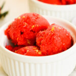 An up-close shot of a small dish of strawberry sorbet garnished with lemon zest.