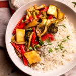 An overhead shot of a white bowl of maple teriyaki tofu and veggies garnished with chopped cilantro.