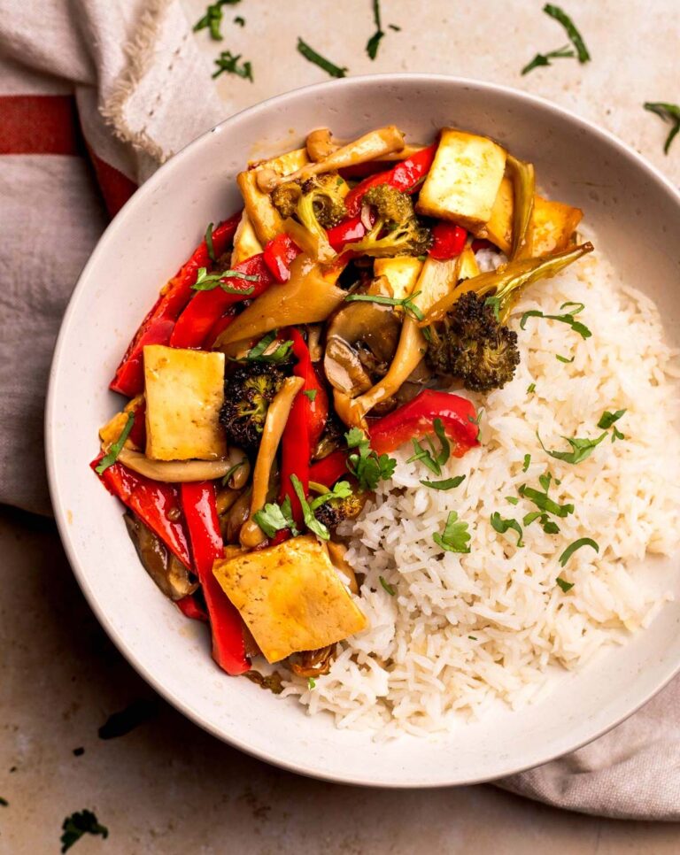 An overhead shot of a white bowl of maple teriyaki tofu and veggies garnished with chopped cilantro.