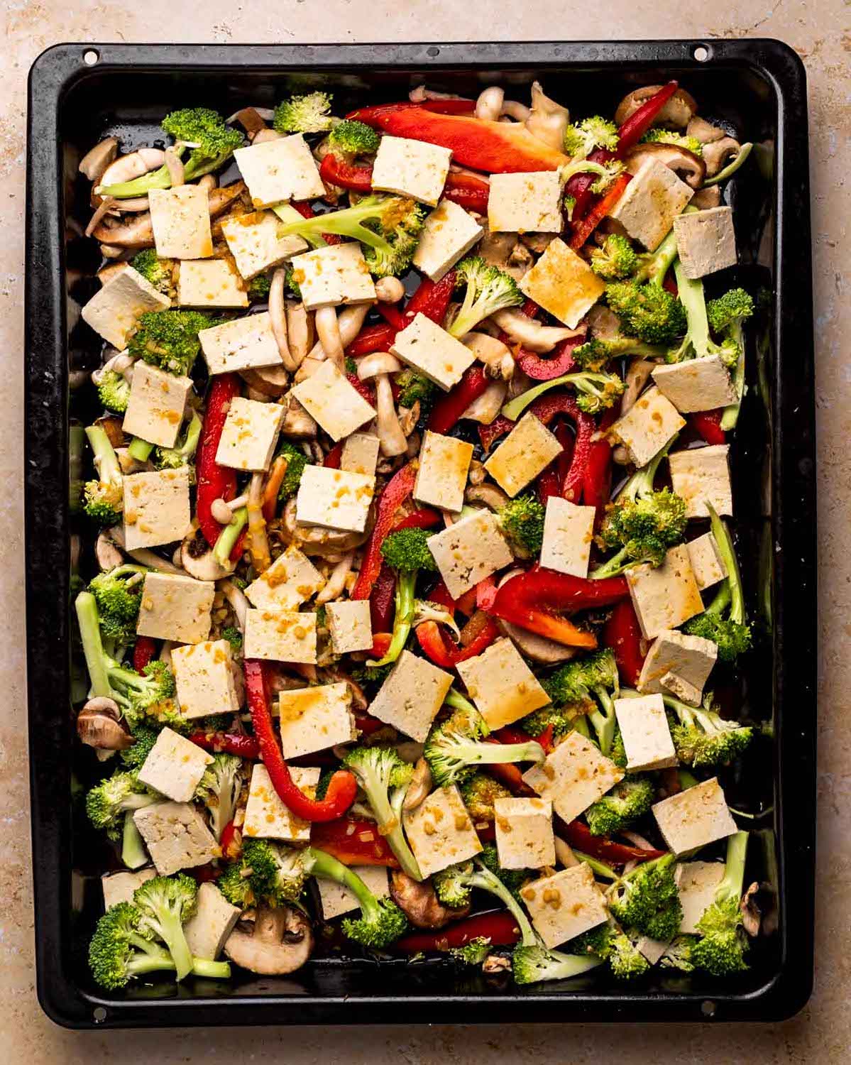 An overhead shot of a baking sheet of veggies with sliced tofu pieces.