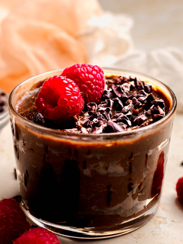 An up-close side shot of a small dish of the vegan chocolate pudding topped with carob chips and raspberries.