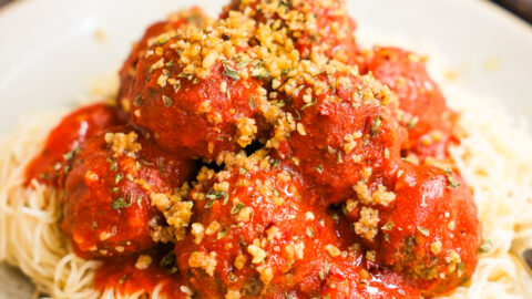 Vegan meatballs stacked on a bed of spaghetti.