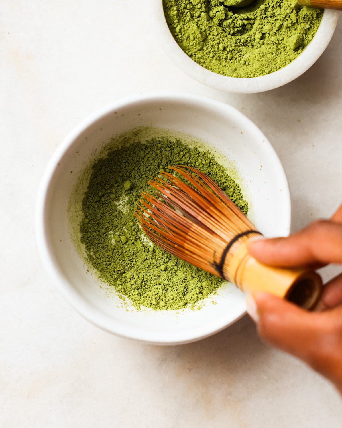 A brown hand whisking a small bowl of matcha.