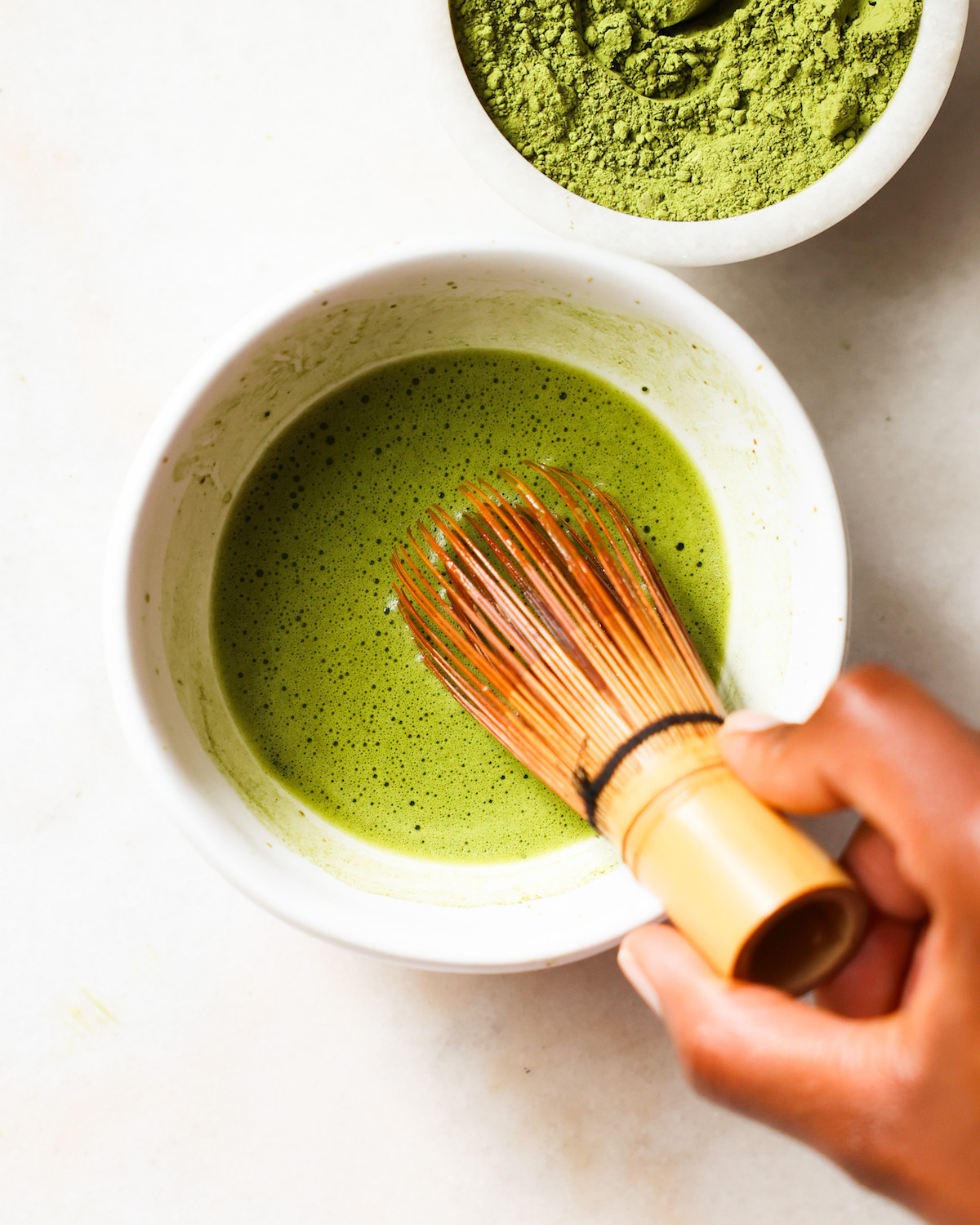 A brown hand whisking a small bowl of matcha and hot water.