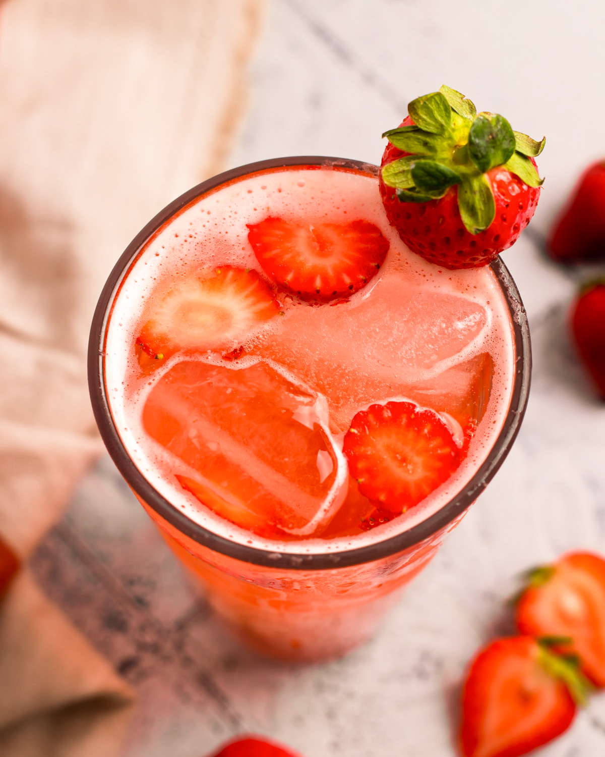 A close-up angled overhead shot of a tall glass of strawberry soda.