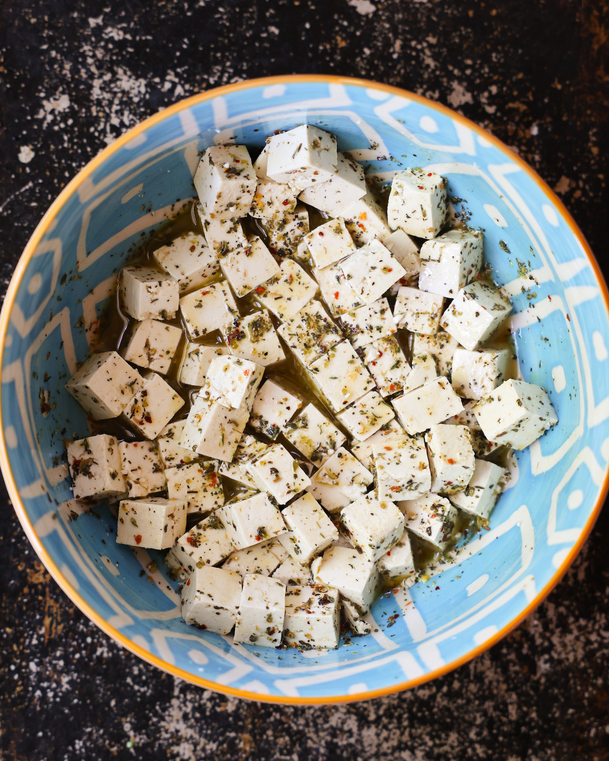 An overhead shot of a blue patterned bowl of marinating tofu cubes.