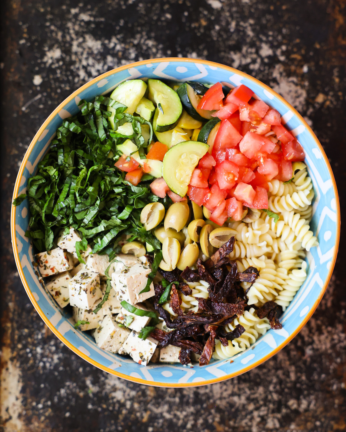 An overhead shot of a patterned blue bowl with pasta, veggies, and marinated tofu.