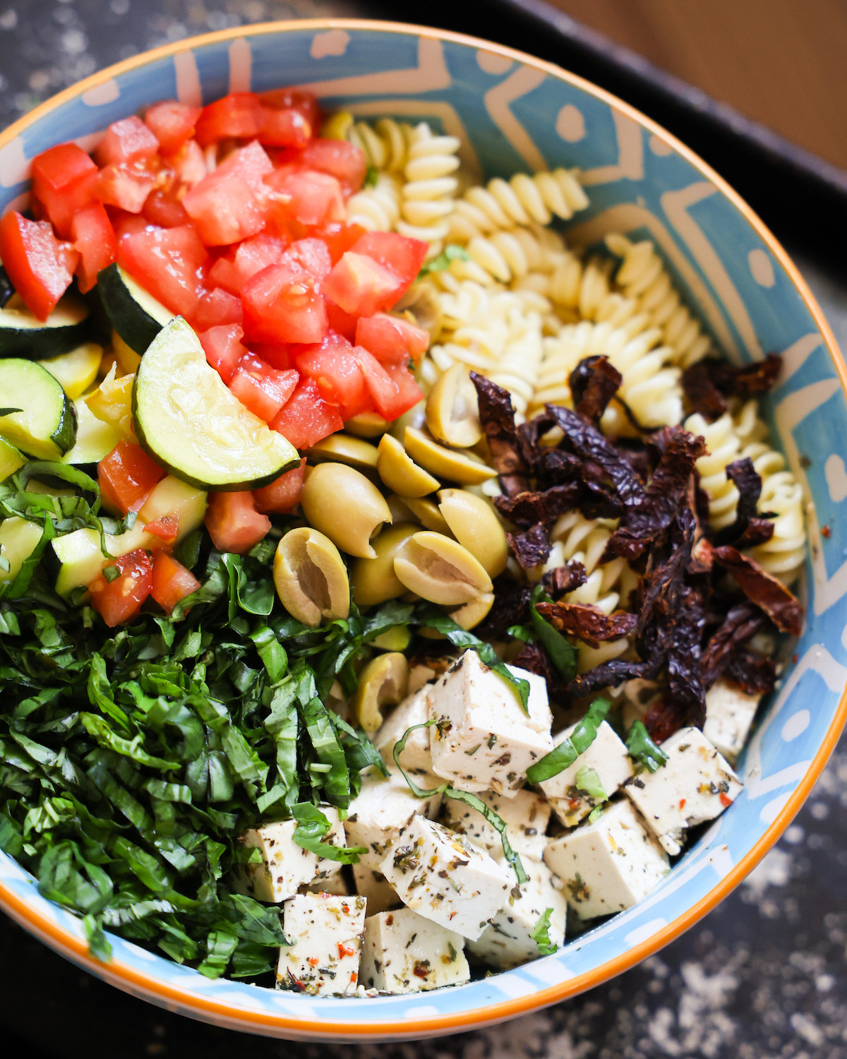 An up-close side shot of a blue patterned bowl of Mediterranean pasta salad.