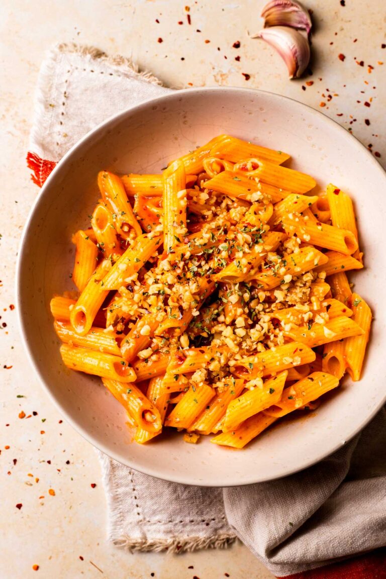 An overhead shot of a white bowl of arrabbiata sauce on penne pasta.