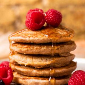 An up-close side shot of a small stack of spelt pancakes with raspberries and maple syrup.