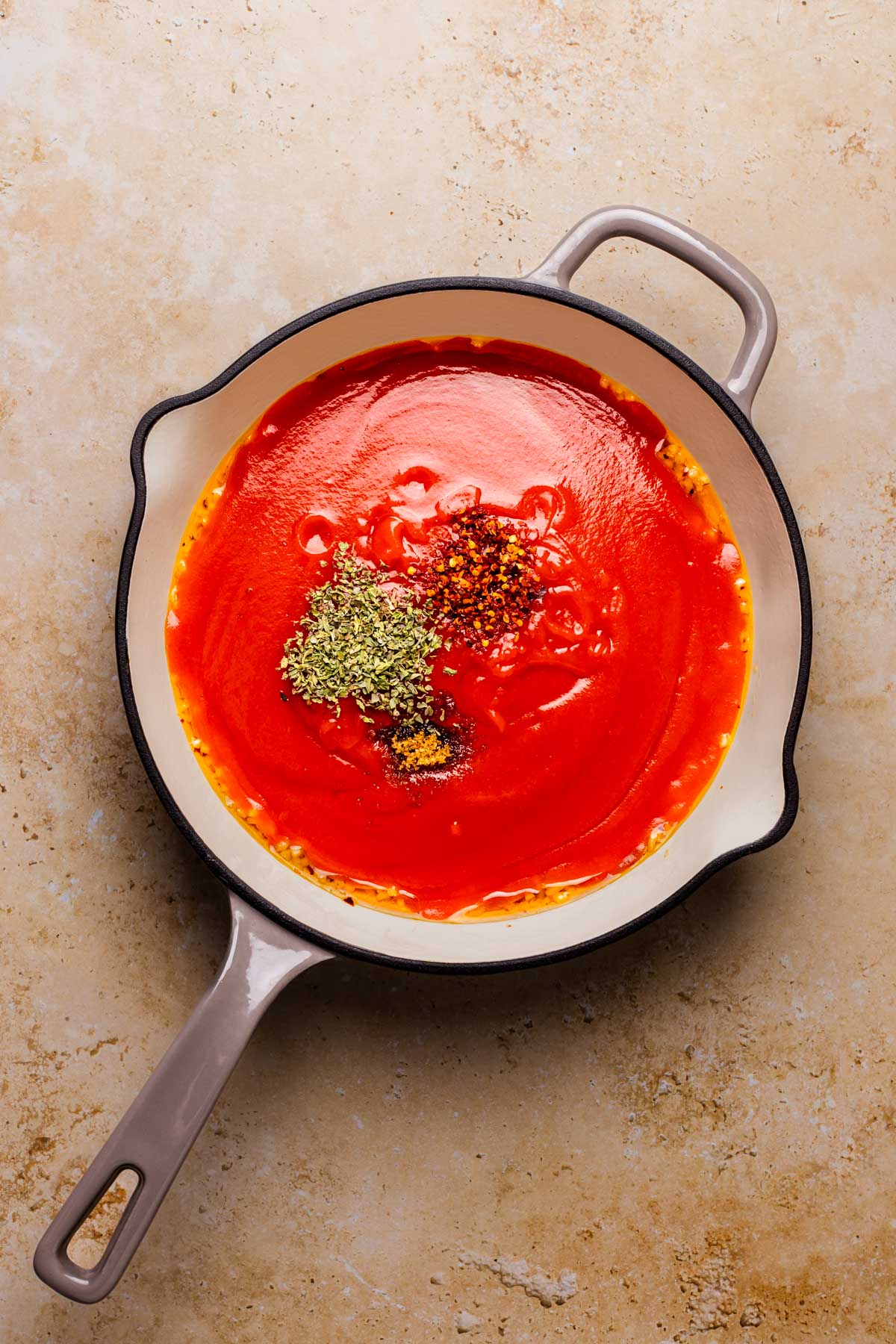 An overhead shot of a skillet with tomato sauce, sauteed garlic, red pepper flakes, and seasonings.