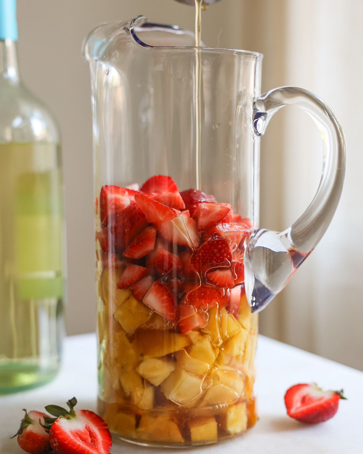Pouring brandy into a pitcher with strawberries and pineapple.