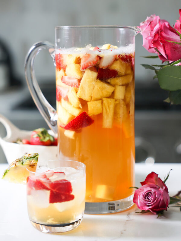 A pitcher and small glass of pineapple summer sangria on the counter with roses.