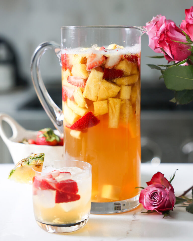 A pitcher and small glass of pineapple summer sangria on the counter with roses.