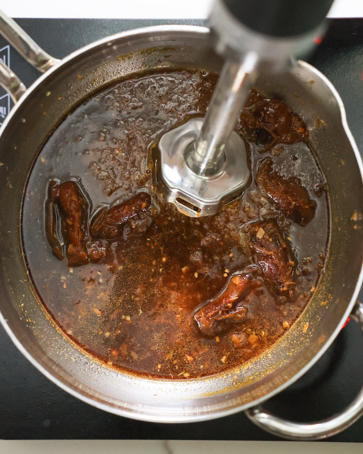 Adding an immersion blender to the saucepan of orange sauce before blending.