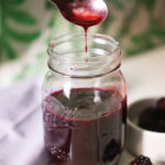 spoon drizzling blackberry syrup over jar