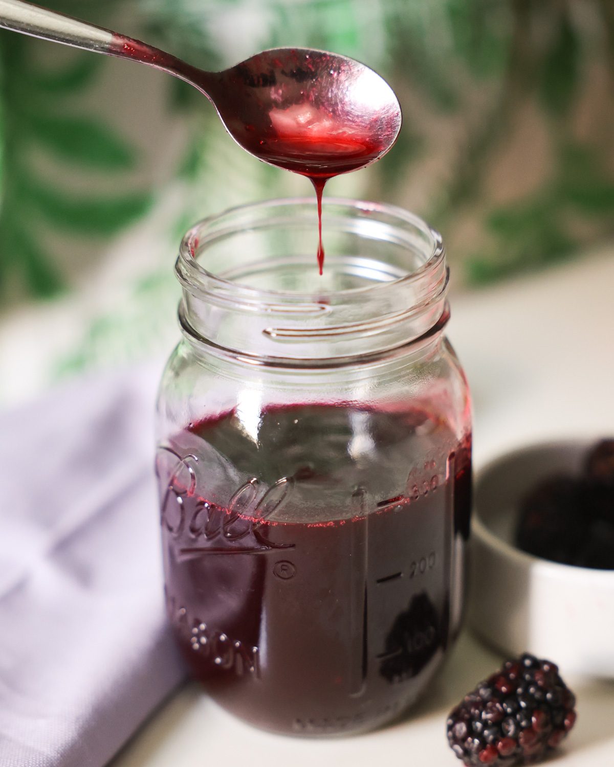 spoon drizzling blackberry syrup over jar