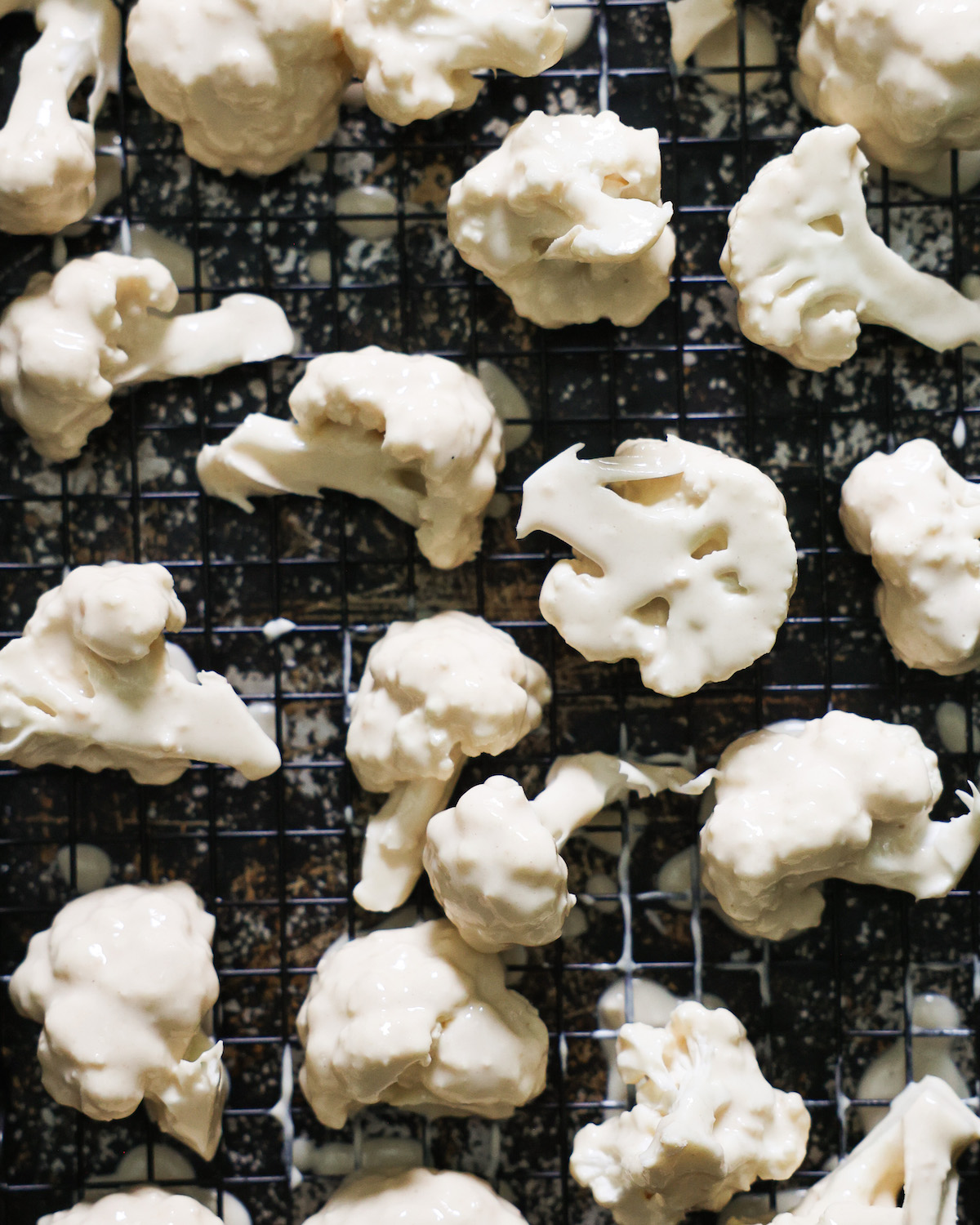 A close-up shot of battered cauliflower on a wire rack-lined baking sheet.