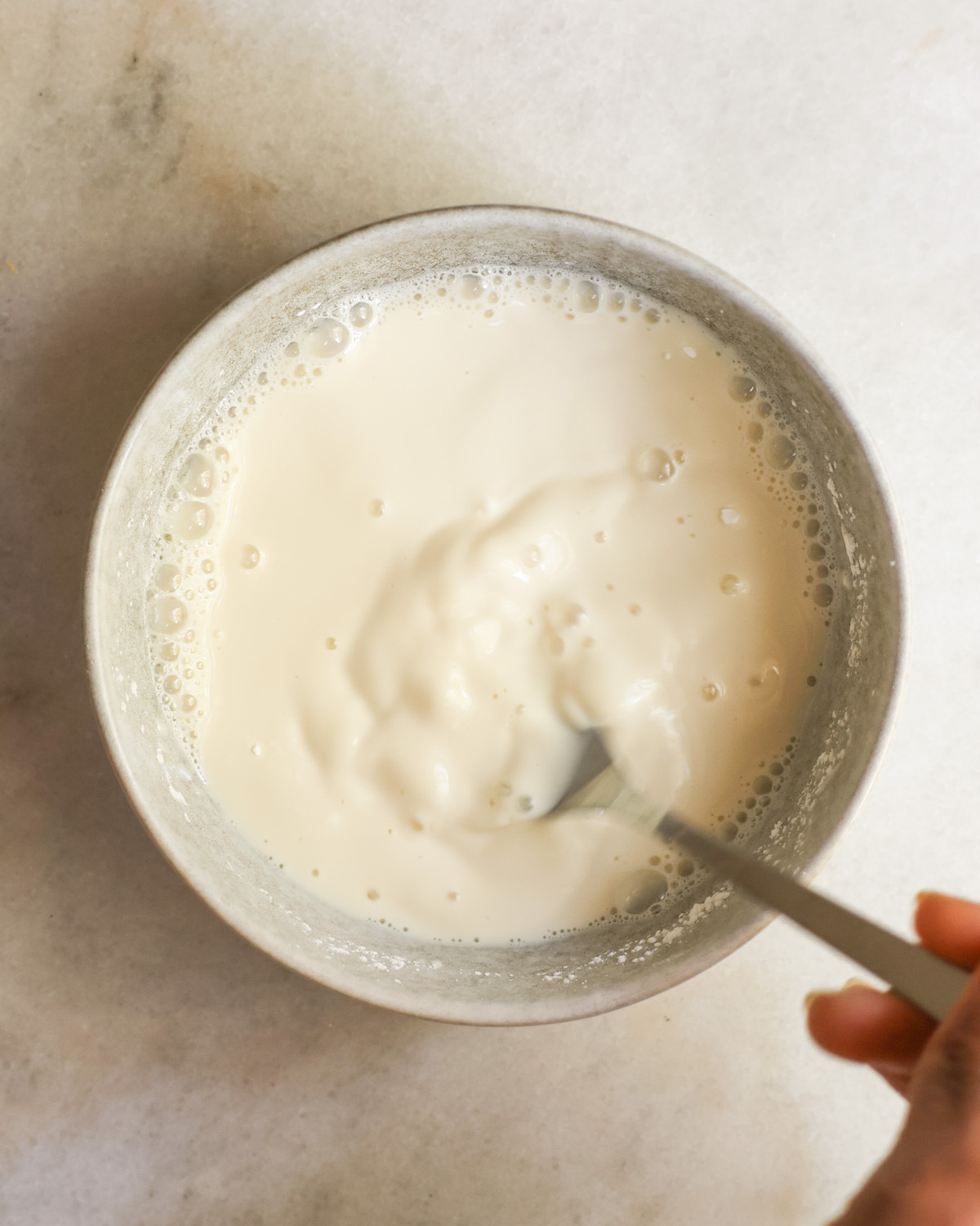 Whisking the arrowroot powder and milk in a grey bowl.