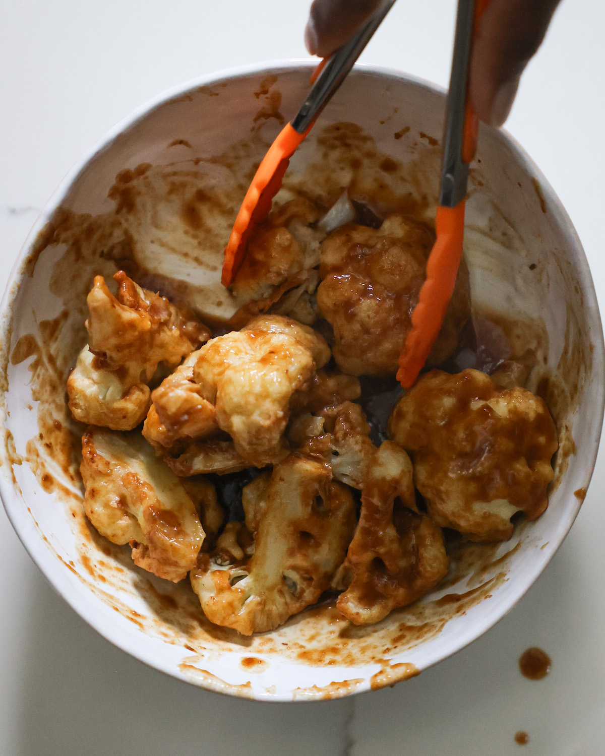 Tossing the cauliflower in the orange sauce in a small mixing bowl.