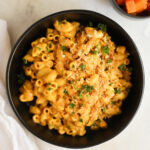 An overhead shot of a black bowl of vegan butternut squash mac and cheese topped with breadcrumbs and minced parsley.