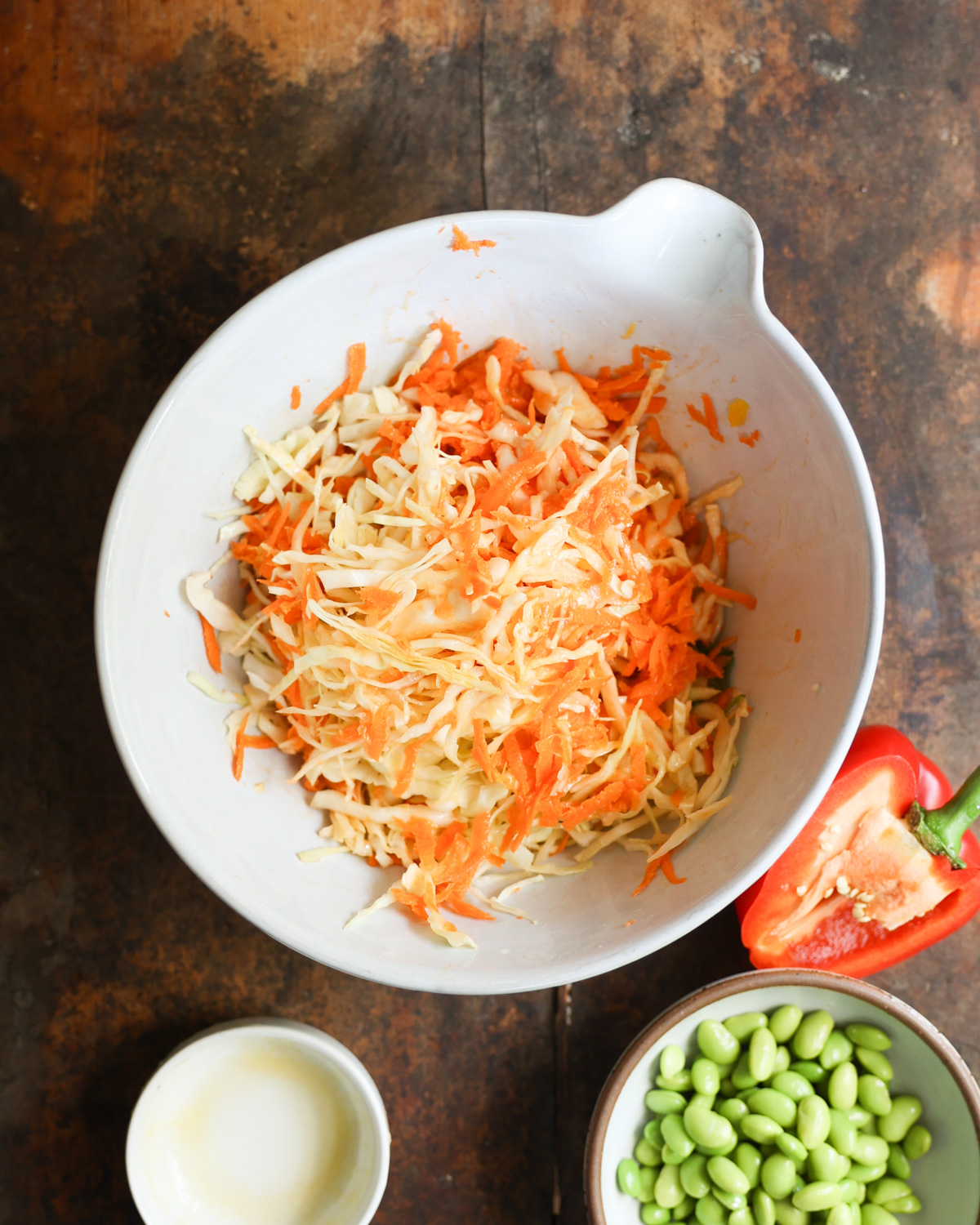 Stirring shredded cabbage and carrots together in a white mixing bowl.